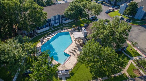 Aerial view of a luxurious apartment complex with a sparkling pool, surrounded by lush greenery and modern buildings.