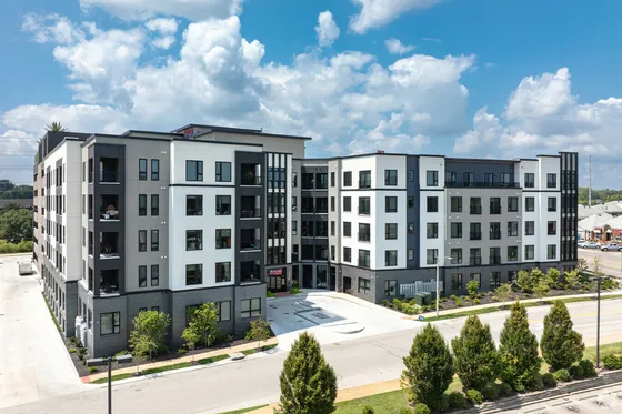 Modern apartment building with sleek design, featuring large windows and landscaped surroundings under a bright blue sky.