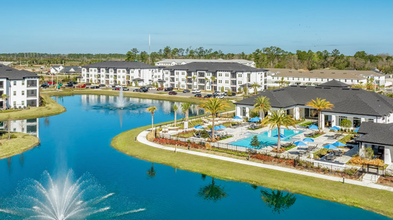 Luxurious apartment complex surrounded by serene lake views, featuring modern architecture, lush landscaping, and a sparkling swimming pool under clear blue skies.