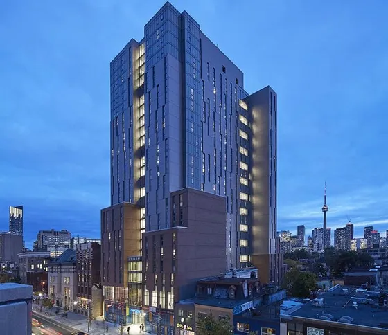 Modern high-rise apartment building illuminated at dusk with city skyline views.