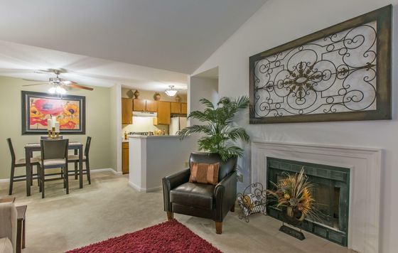 Elegant living area featuring a cozy seating arrangement by the fireplace, a chic dining set with vibrant artwork, and an inviting kitchen with warm wooden cabinetry.