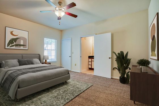 Inviting bedroom with elegant decor, featuring a plush grey bed, stylish artwork, natural light from a window, and a modern ceiling fan.