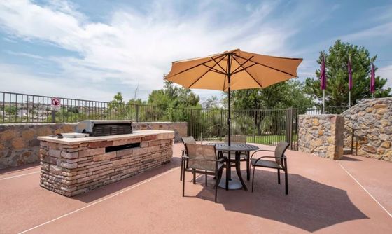 Inviting outdoor patio with a stone BBQ grill and shaded seating, perfect for entertaining under sunny skies.