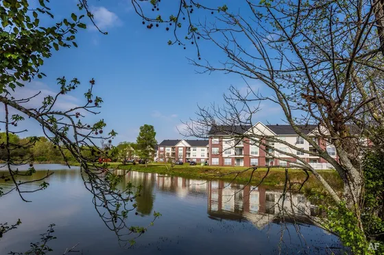 Charming lakeside apartments with picturesque reflections, surrounded by lush greenery and blue skies, offering tranquil living.