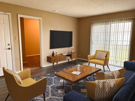 Chic living room with stylish yellow armchairs, modern coffee table, and large TV, bathed in natural light from expansive windows with vertical blinds.
