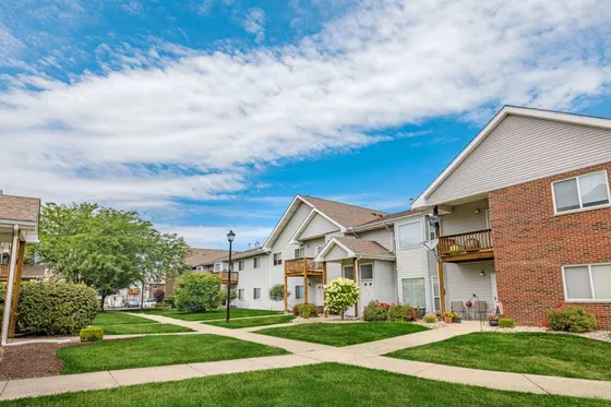 Charming apartment complex with modern architecture, lush green lawns, and a bright blue sky.