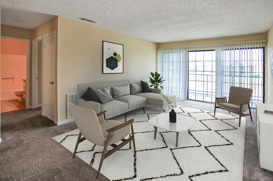 Bright and airy living room with modern decor, featuring a plush gray sofa, chic armchairs, geometric rug, and expansive sliding glass doors offering abundant natural light.