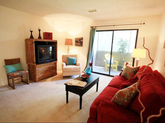 Inviting living room with plush red sofa, wooden accents, and natural light from sliding glass doors leading to a cozy balcony.
