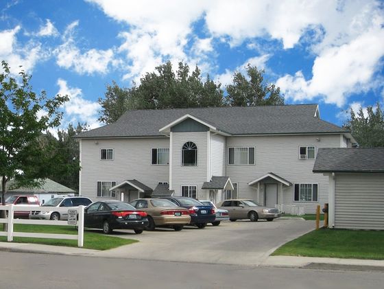Charming suburban apartment complex with modern architecture, ample parking, and lush greenery under a vibrant blue sky.