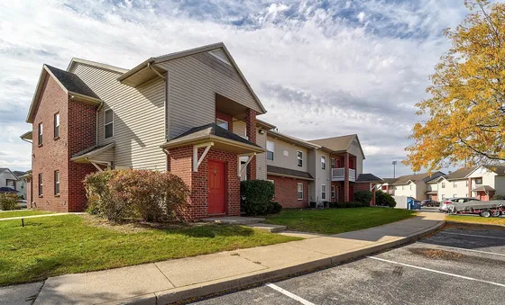 Charming brick apartment complex surrounded by lush greenery, showcasing a sunny autumn ambiance under a vibrant sky.