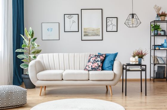 Elegant living room with a modern white sofa, chic floral cushions, artistic wall frames, and ambient lighting.