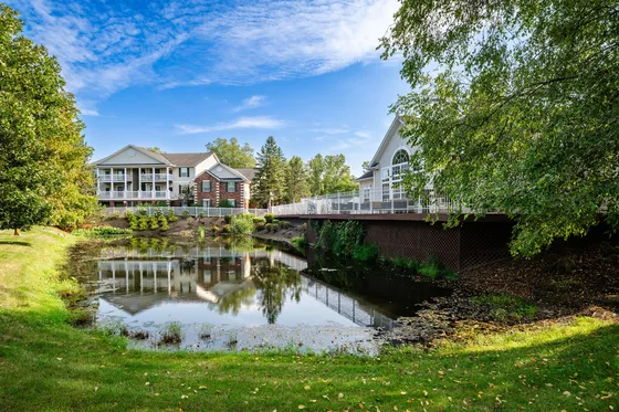 Charming apartment complex with elegant brick facade, scenic pond, and lush greenery under a vibrant blue sky.