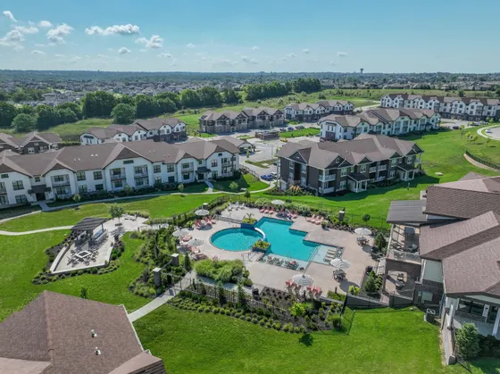 Aerial view of luxurious apartment complex with beautifully landscaped gardens and a sparkling swimming pool surrounded by sun loungers and umbrellas, offering a serene and upscale living experience.