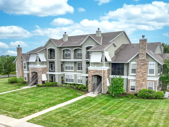 Charming apartment complex with elegant stone facades, spacious balconies, and lush green lawns under a bright blue sky.