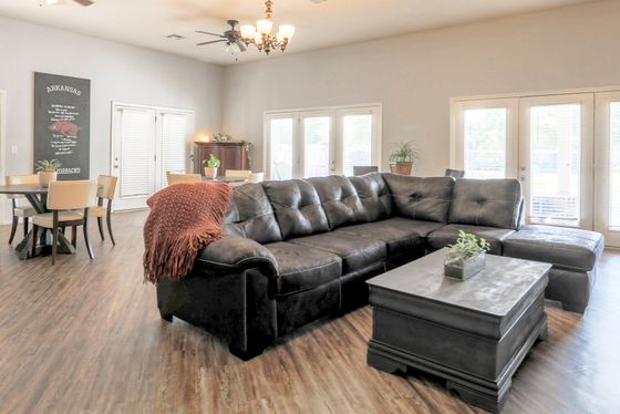 Spacious living area with elegant dark leather sectional sofa, cozy wooden coffee table, dining nook, and abundant natural light from large windows.