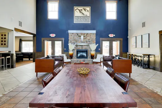 Inviting apartment common area featuring a stylish wooden table, cozy leather seating, and a stone fireplace under a high ceiling.
