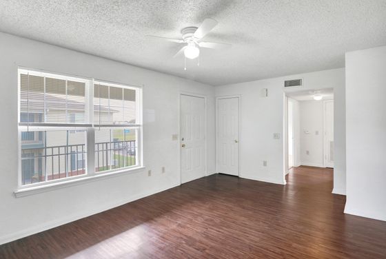 Bright and inviting room with elegant hardwood floors, large windows offering natural light, and a ceiling fan for comfort.