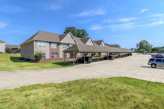 Charming apartment complex with covered parking, spacious grassy areas, and bright blue skies.