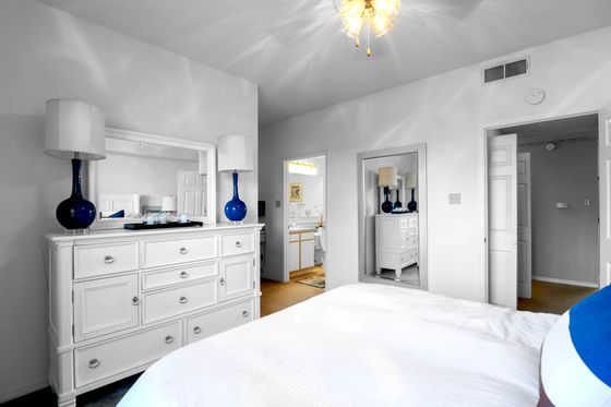 Chic bedroom with elegant white furniture, vibrant blue accents, and a cozy ambiance.