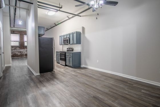 Modern apartment interior featuring sleek kitchen with blue cabinets, stainless steel appliances, and stylish wood flooring, boasting an industrial chic vibe with exposed brick and pipes.