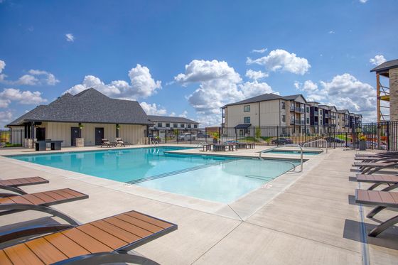 Luxurious apartment complex with a pristine swimming pool, sun loungers, and modern architectural design under a bright blue sky.