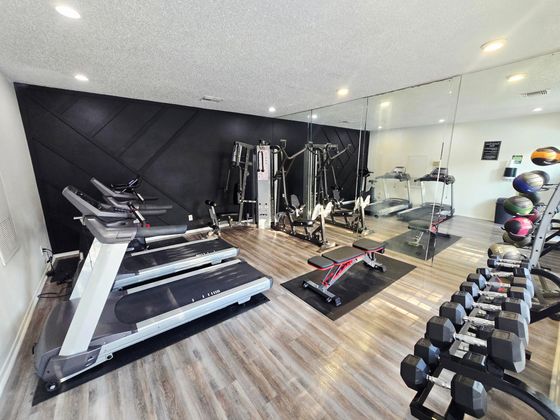 Modern fitness center featuring state-of-the-art treadmills, versatile weight machines, and a selection of free weights, equipped with sleek wood flooring and wall mirrors.