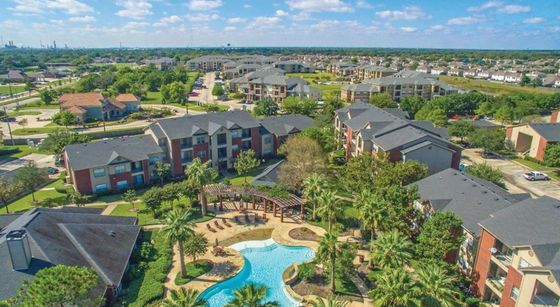Vibrant aerial view of a luxurious apartment community with beautifully landscaped gardens, resort-style pool, and modern apartment buildings.