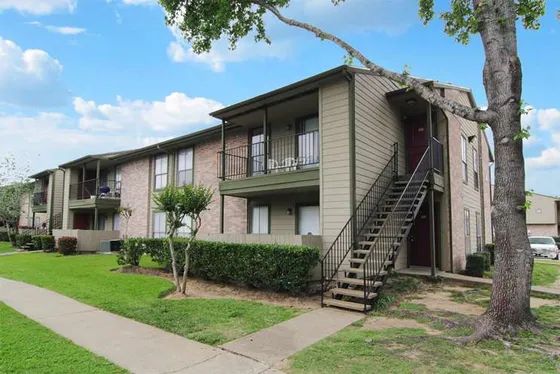 Charming apartment exterior with private balconies, surrounded by lush greenery and a serene pathway.