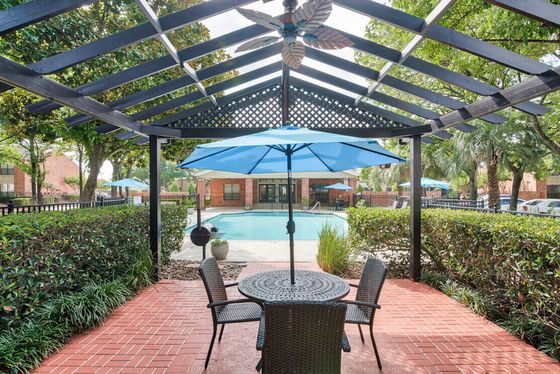 Charming outdoor patio with a blue umbrella overlooking a serene pool surrounded by lush greenery.