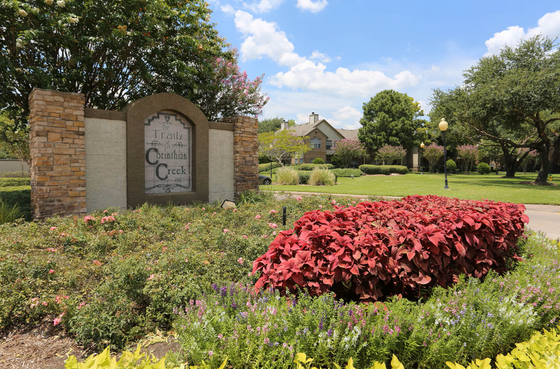 Lush landscape featuring vibrant flowerbeds and a welcoming stone entrance sign at Corinthian Creek apartments.