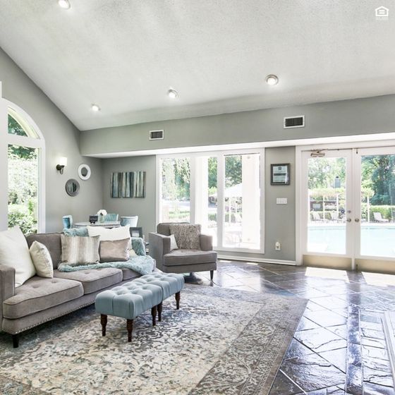 Bright and airy living room with elegant decor, featuring a plush gray sofa, stylish armchair, and floor-to-ceiling windows opening to a scenic pool view.