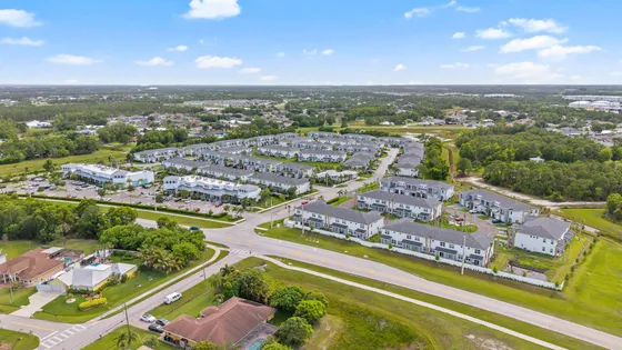 Expansive aerial view of a vibrant residential community surrounded by lush greenery, showcasing modern townhouses and convenient amenities.