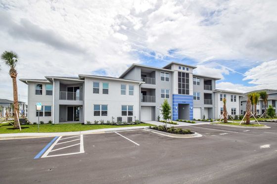 Modern apartment complex with sleek design, spacious balconies, and lush landscaping under a bright sky.