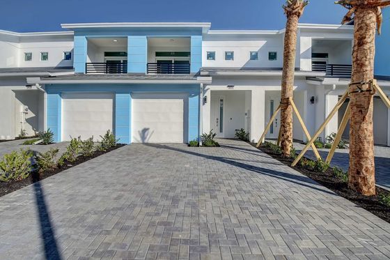 Modern duplex with a contemporary facade, featuring stunning blue accents, a spacious paved driveway, and elegant palm trees.
