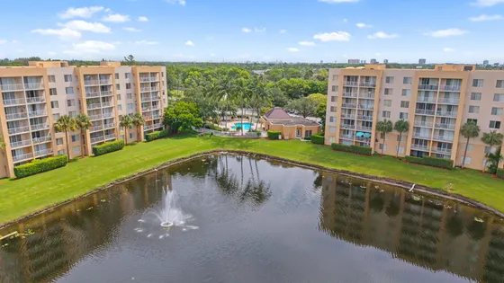 Vibrant aerial view of stylish apartment buildings with balconies overlooking a serene pond and fountain, surrounded by lush greenery and a luxurious pool area.