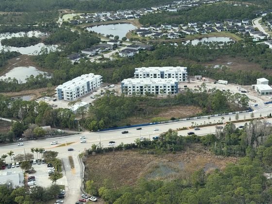 Aerial view of a modern apartment complex surrounded by lush greenery and tranquil ponds, offering a serene living environment with easy access to nearby amenities.