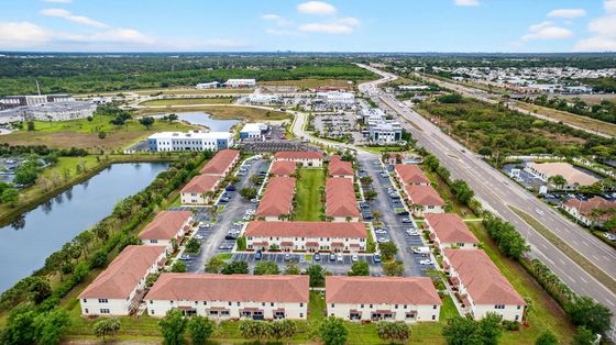 Aerial view of a charming apartment complex with red-roofed buildings, ample parking, and scenic pond views, offering convenient access in a lush green setting.