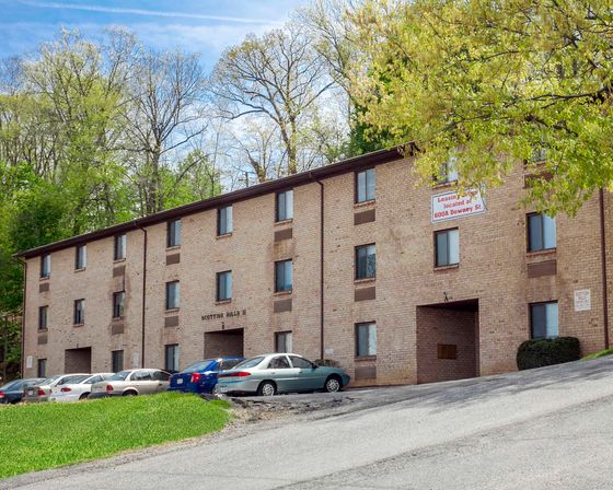 Inviting brick apartment building nestled in a lush green setting with ample parking, offering a tranquil yet convenient living experience.