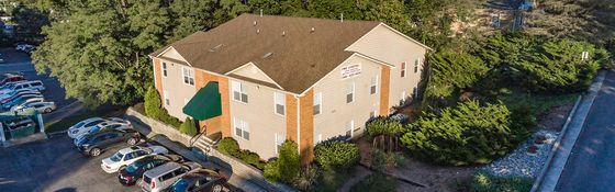 Charming aerial view of a cozy apartment building nestled among lush greenery with ample parking space, conveying a sense of community and convenience.