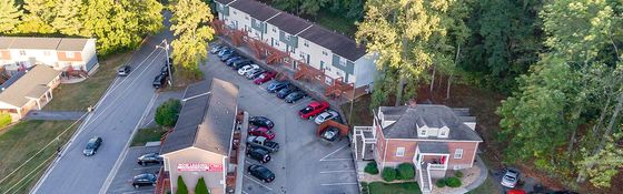 Charming aerial view of a well-maintained apartment complex surrounded by lush greenery, offering ample parking and vibrant community living.