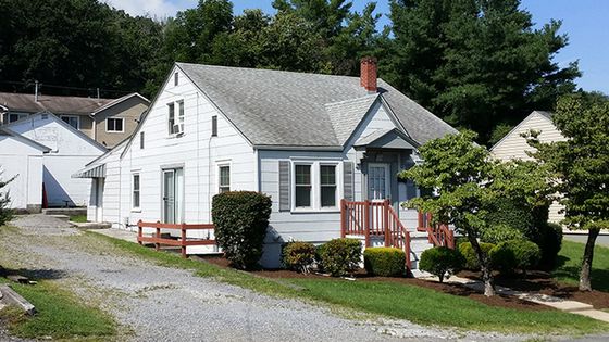 Charming suburban home with a welcoming front porch, lush green landscaping, and a gravel driveway.