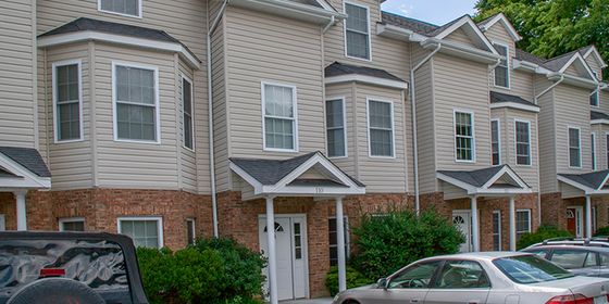 Charming townhouse exterior with classic architecture, featuring bay windows and a cozy entrance, surrounded by lush greenery and convenient parking.