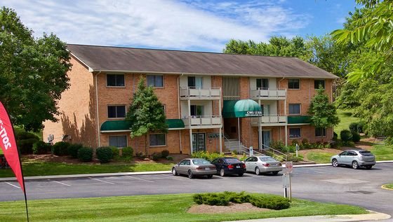 Charming brick apartment complex with green awnings, surrounded by lush landscaping and ample parking space.