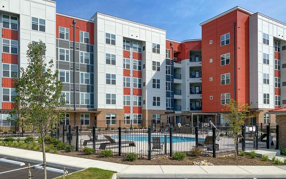 Modern apartment complex featuring a vibrant facade with expansive windows, landscaped surroundings, and a refreshing outdoor swimming pool.