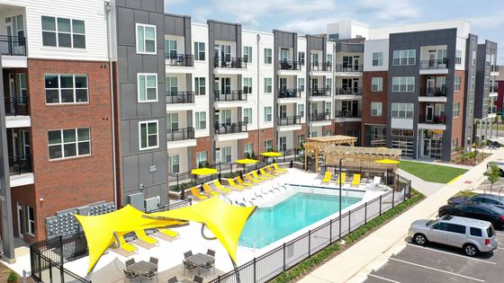 Modern apartment complex with stylish balconies, inviting swimming pool area, and vibrant yellow lounge chairs, offering a luxurious lifestyle.