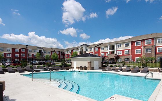 Charming apartment complex featuring a sparkling outdoor pool, surrounded by modern buildings and lush greenery, perfect for upscale living.