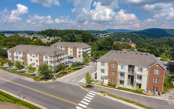 Charming apartment complex nestled in lush greenery, featuring modern architecture and scenic mountain views under a bright blue sky.