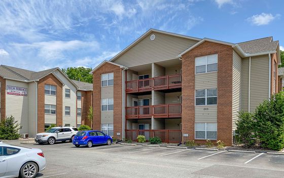 Charming apartment complex featuring spacious 4-bedroom units, with a welcoming facade and ample parking under a clear blue sky.