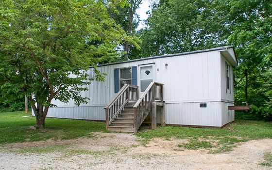 Charming mobile home nestled amidst lush greenery, featuring an inviting wooden staircase leading to the entrance.