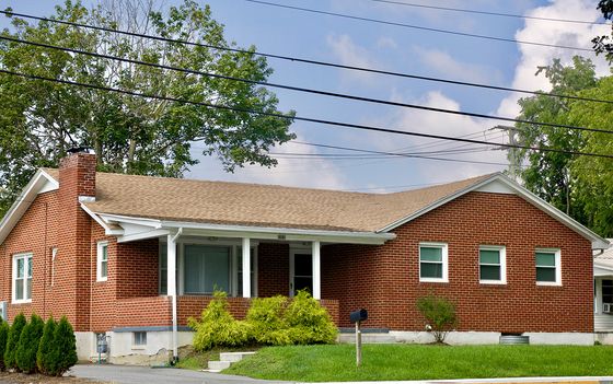 Charming single-story brick house with a welcoming front porch, nestled in a lush green setting.